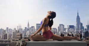 A woman practicing yoga split pose on a rooftop overlooking the NYC skyline at a group exercise gym